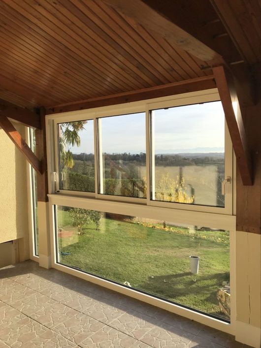 Véranda avec plafond en bois et grandes fenêtres donnant sur un paysage verdoyant au coucher du soleil