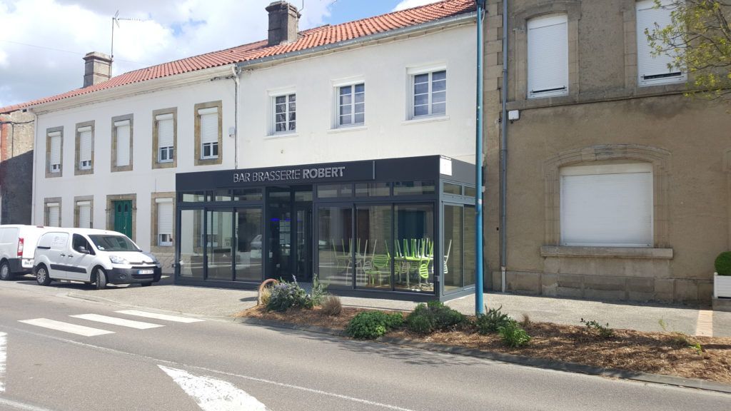 Vue sur rue d’une rangée de bâtiments blancs avec un commerce au rez-de-chaussée et une voiture garée à gauche