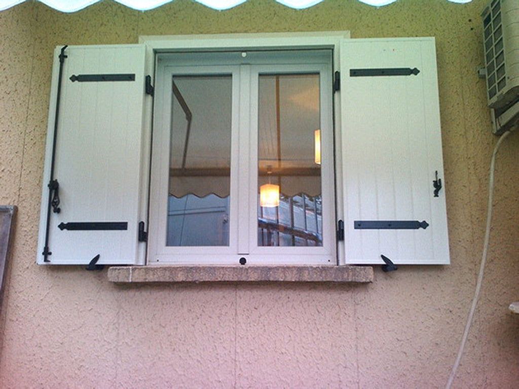 Fenêtre blanche aux volets ouverts sur un mur en stuc beige