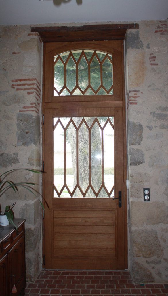 Porte d’entrée en bois avec panneaux décoratifs en verre dépoli, intégrée dans un mur en pierre