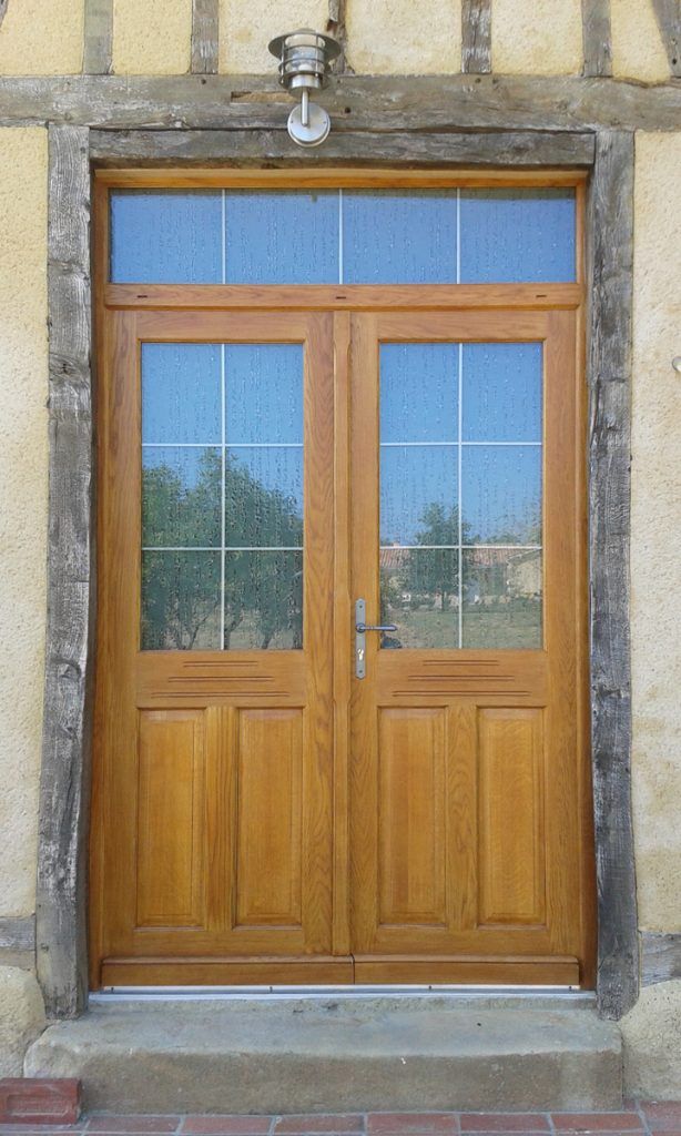 Porte en bois à deux vantaux avec des panneaux vitrés, intégrée à la façade d’un bâtiment en pierre