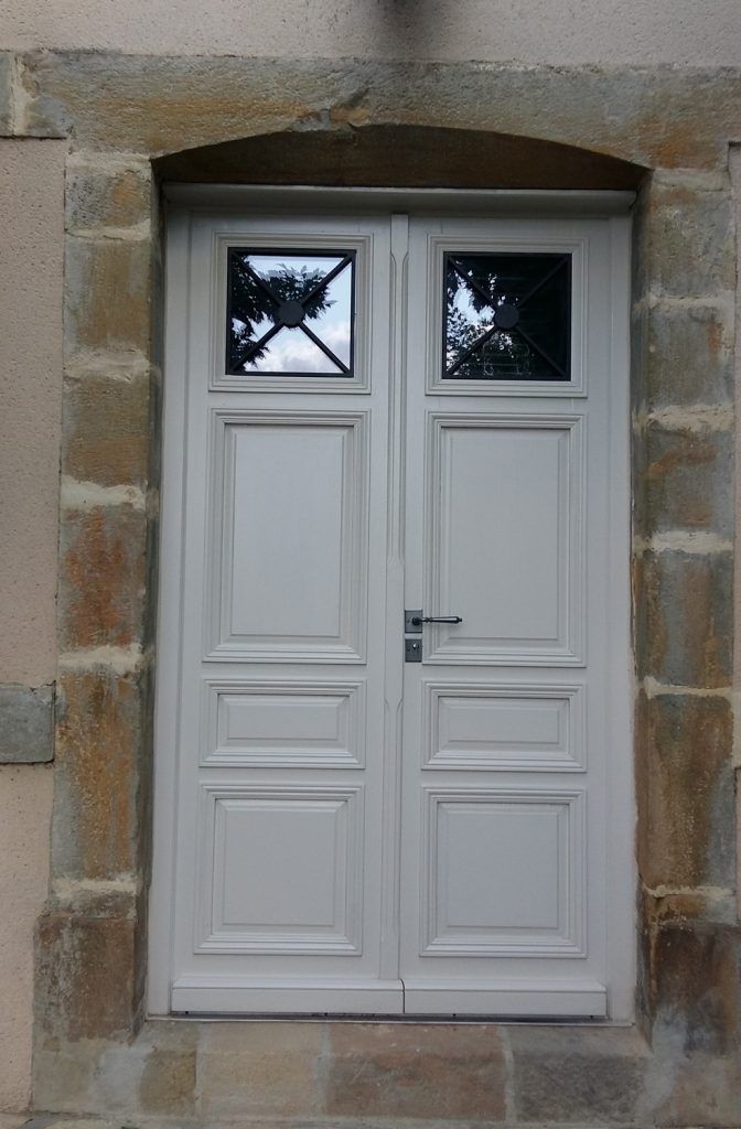 Porte double blanche avec de petites fenêtres, encastrée dans un mur en pierre