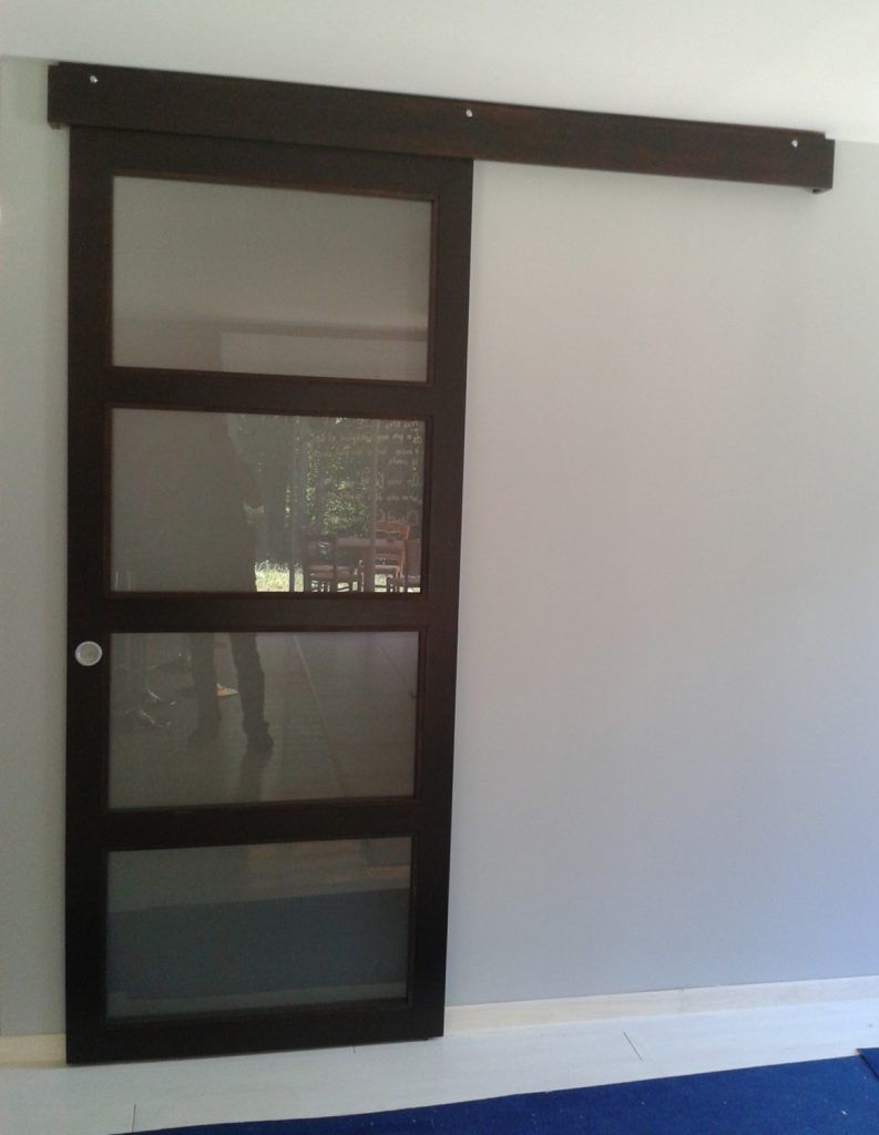 Porte coulissante de grange en bois foncé, avec des panneaux en verre dépoli, sur un mur blanc.