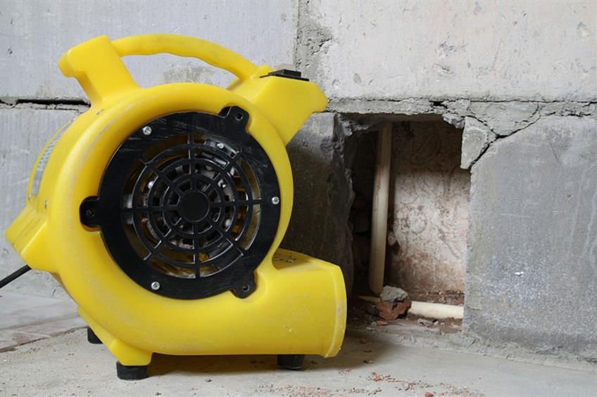 Ein gelbes Gebläse steht auf dem Boden neben einer Backsteinmauer.