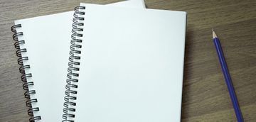 Dos cuadernos de espiral y un lápiz sobre una mesa de madera.