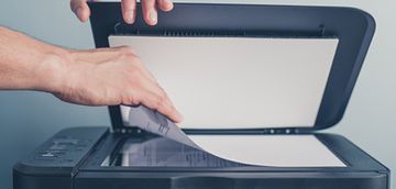 Una persona está usando una impresora para escanear una hoja de papel.