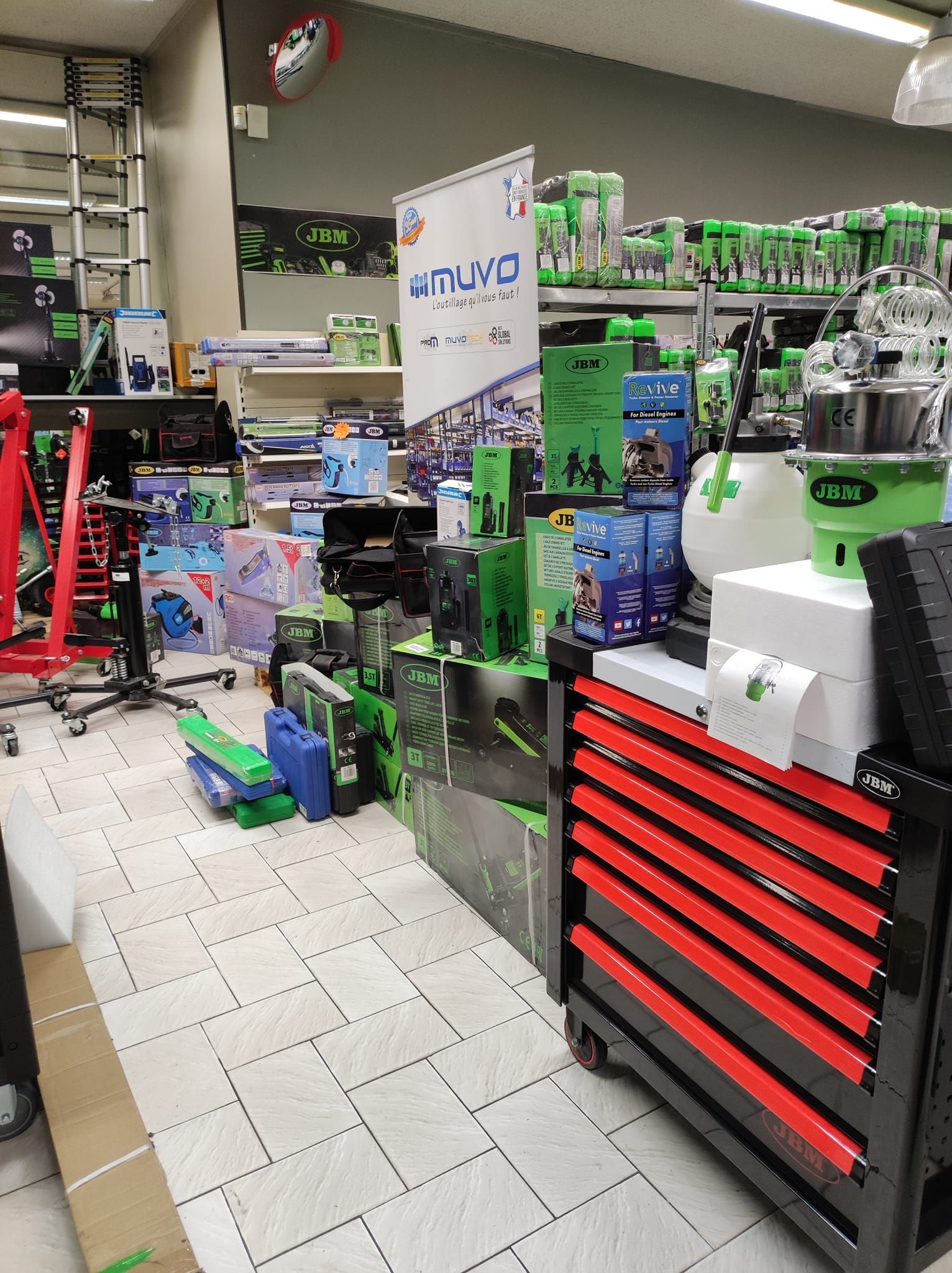 Une allée de magasin avec, au premier plan, une caisse à outils rouge et des étagères remplies d'outils et d'équipements.