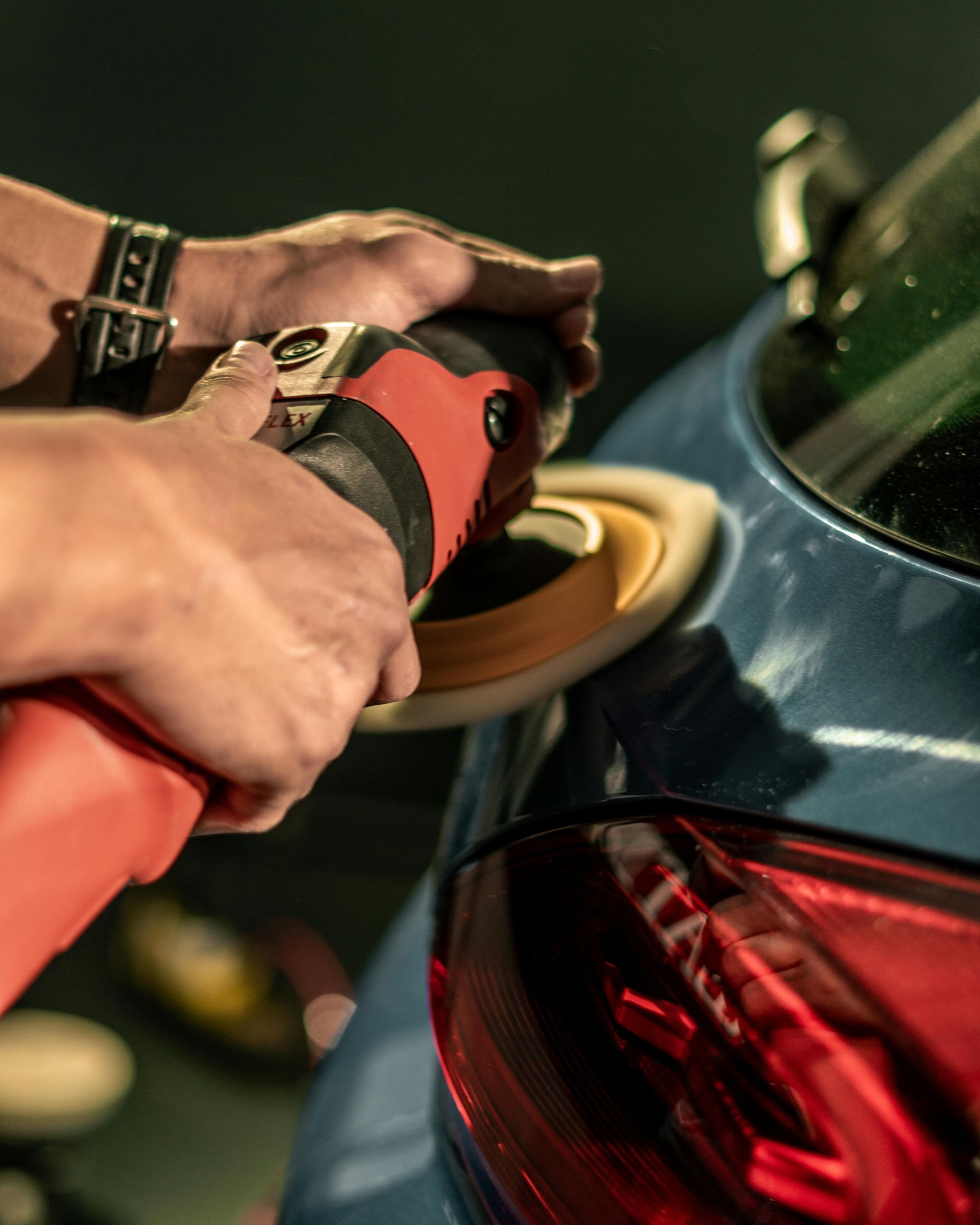Gros plan sur une personne utilisant une polisseuse électrique rouge pour polir la carrosserie bleue d'un véhicule.