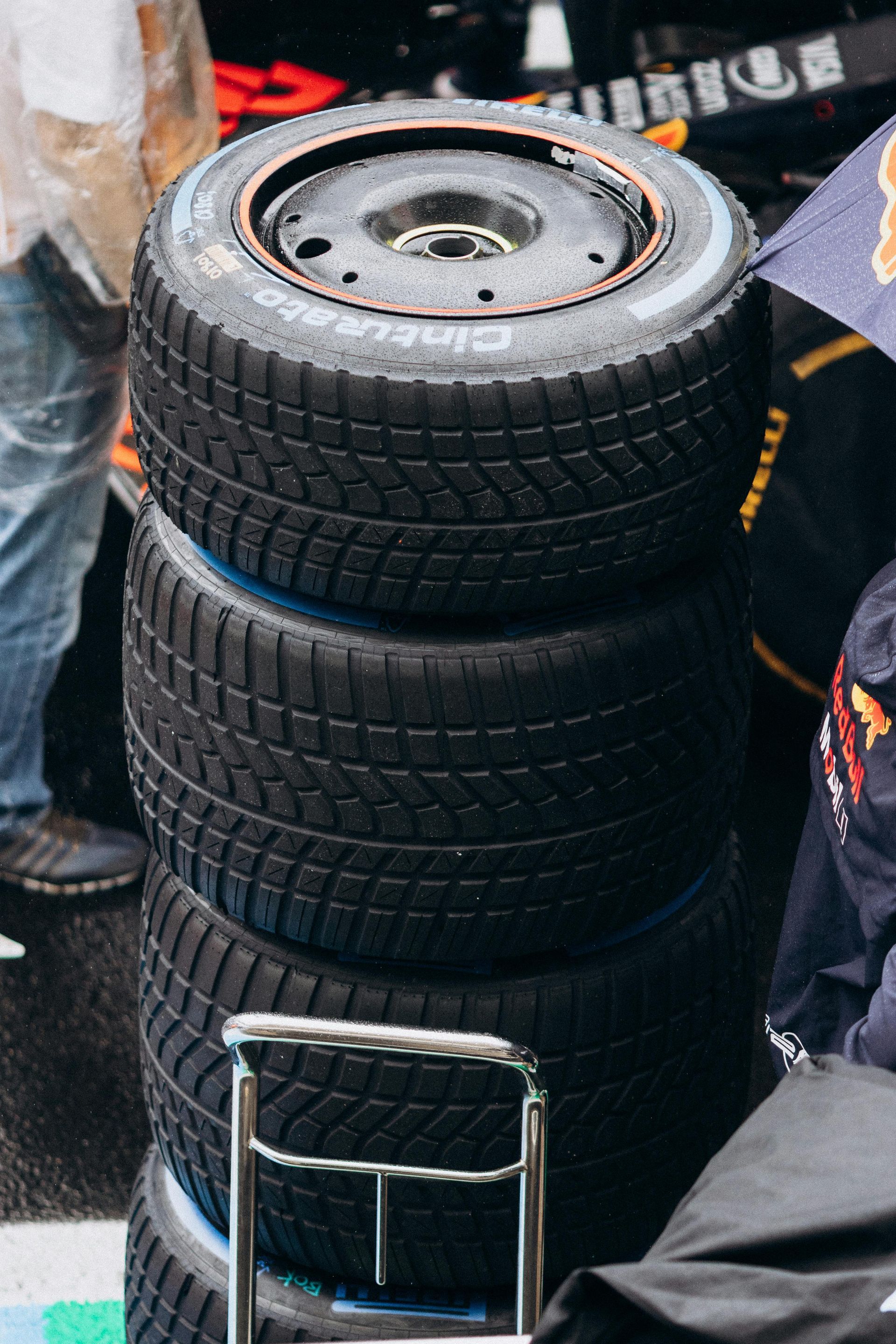 Une pile verticale de quatre pneus Pirelli de Formule 1 pour temps humide, avec un marquage bleu, posés sur un support dans la voie des stands.