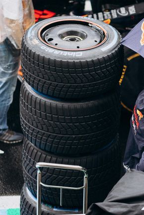 Une pile verticale de quatre pneus Pirelli de Formule 1 pour temps humide, avec un marquage bleu, posés sur un support dans la voie des stands.