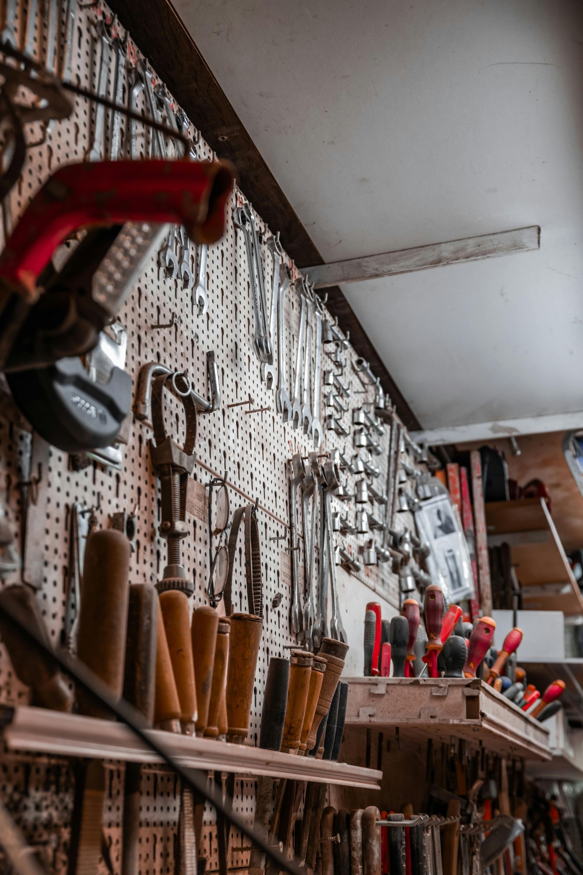 Panneau perforé mural d'atelier rempli de divers outils à main en métal suspendus, de clés et de ciseaux à bois.