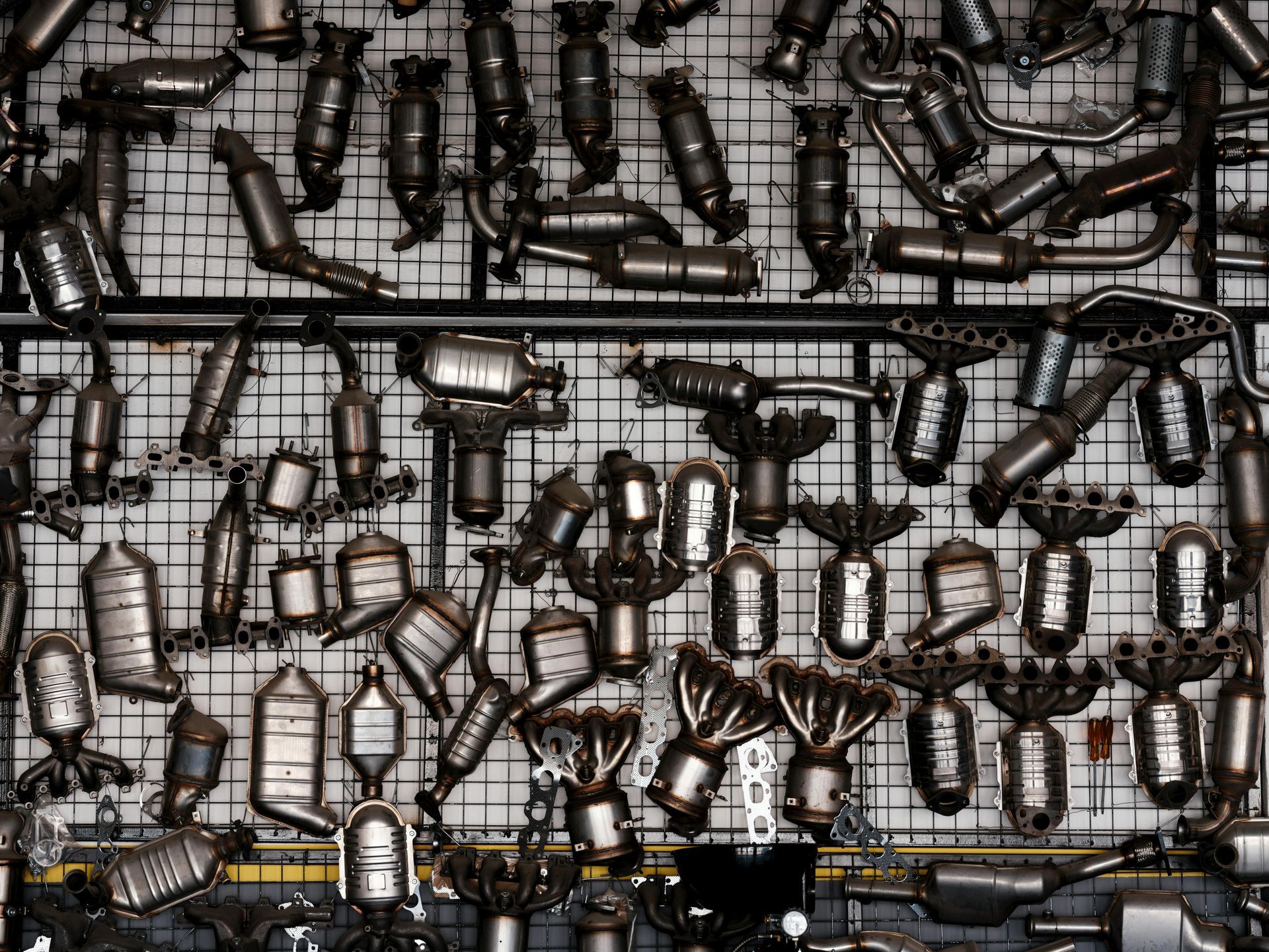 De nombreux pots catalytiques automobiles sont suspendus à une grille métallique murale dans un entrepôt.