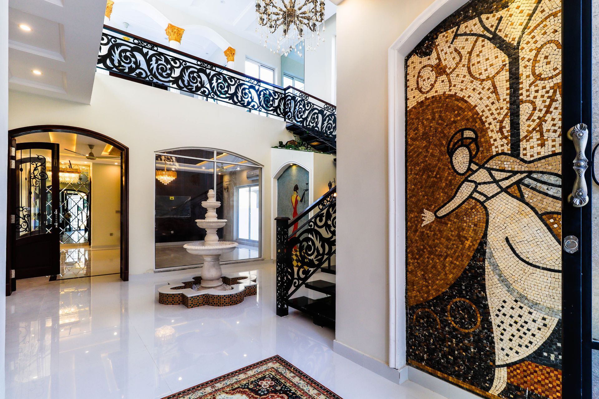 Elegant foyer with mosaic wall art, black wrought-iron staircase, and white fountain in a bright glossy interior
