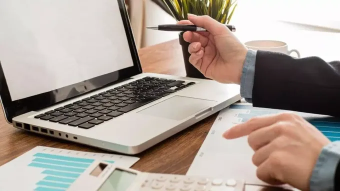 Una persona apunta a una computadora portátil mientras sostiene un bolígrafo.