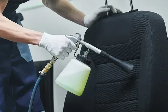 Un hombre está limpiando el asiento de un automóvil con una botella de spray.