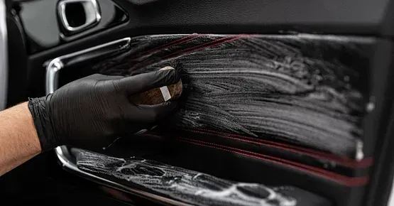Una persona está limpiando el interior de la puerta de un coche con un cepillo.