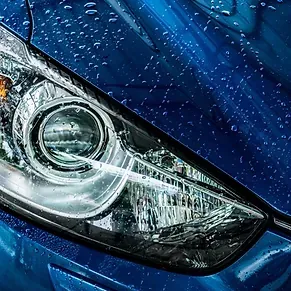 Un primer plano del faro de un coche azul con gotas de agua sobre él.