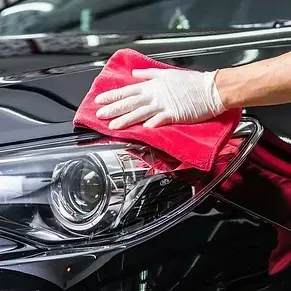 Una persona está limpiando el faro de un coche con una toalla roja.