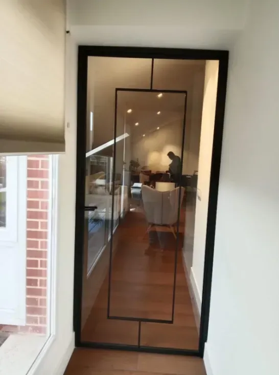 Una puerta de cristal conduce a un comedor con iluminación cálida, con sillas y una mesa, más allá de la entrada.