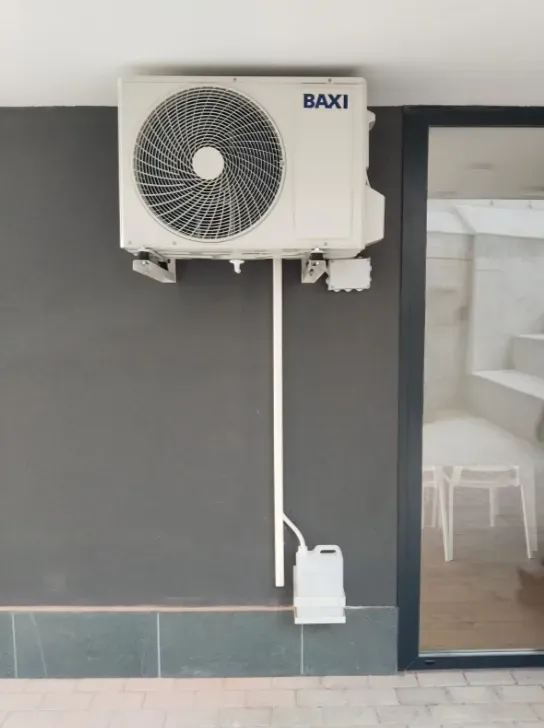 Unidad exterior de aire acondicionado BAXI montada en la pared junto a una puerta de cristal