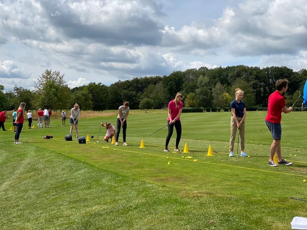 Auf einer grasbewachsenen Wiese mit gelben Hütchen standen Menschen Schlange und übten den Abschöag beim Golf