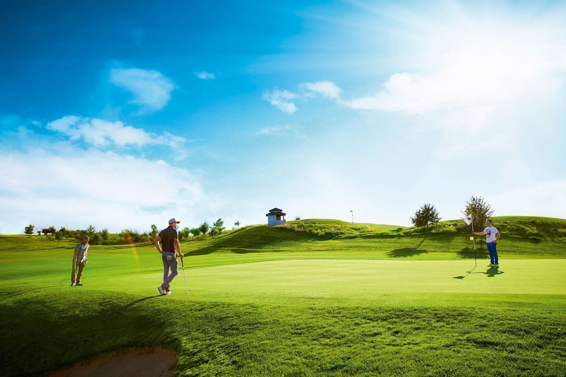Golfer auf einem leuchtend grünen Platz unter blauem Himmel mit Wolken