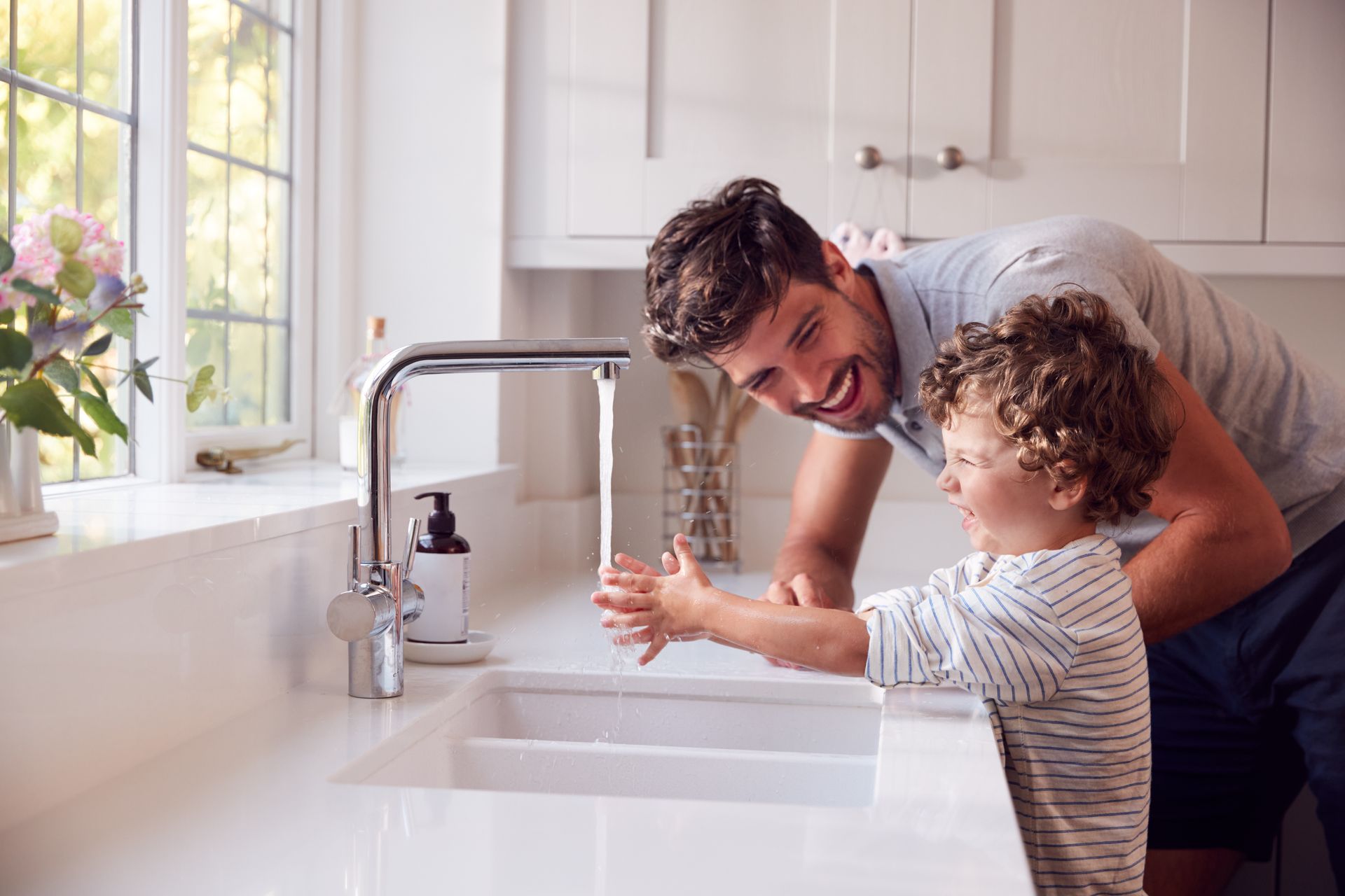 Un père et son fils avec l'eau qui coule du robinet de cuisine.