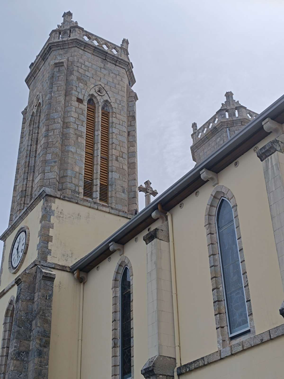 Torre de iglesia de piedra con reloj y altas ventanas arqueadas contra un cielo gris.