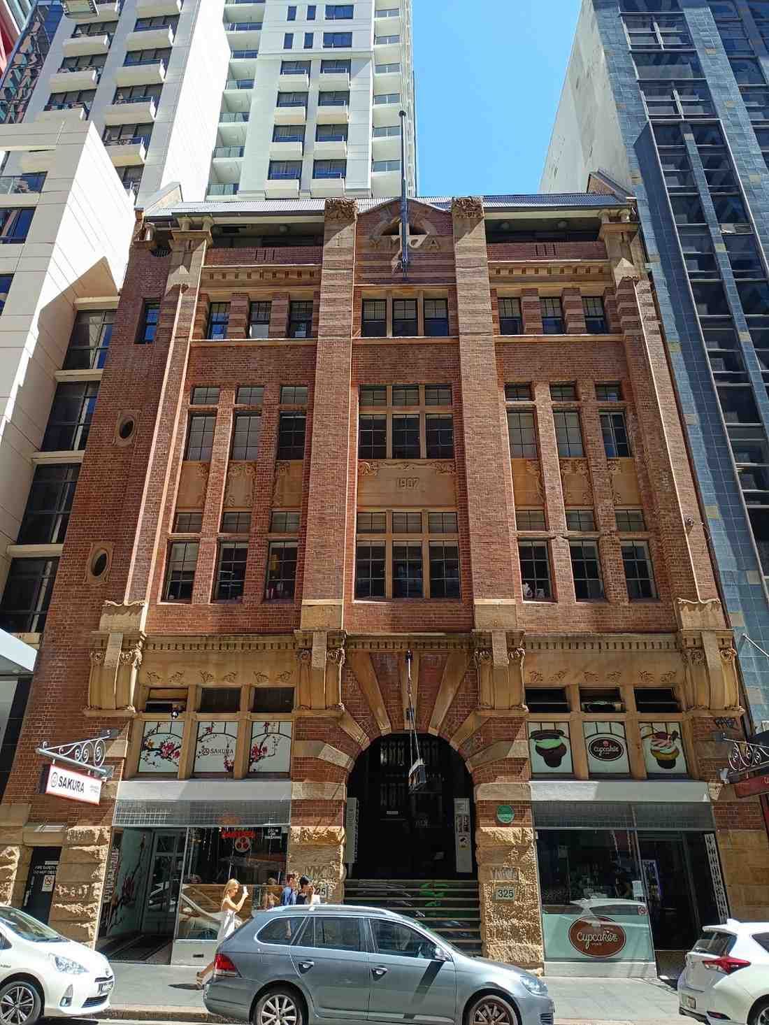 Edificio histórico de ladrillo rojo con entrada arqueada y locales comerciales en una calle de la ciudad