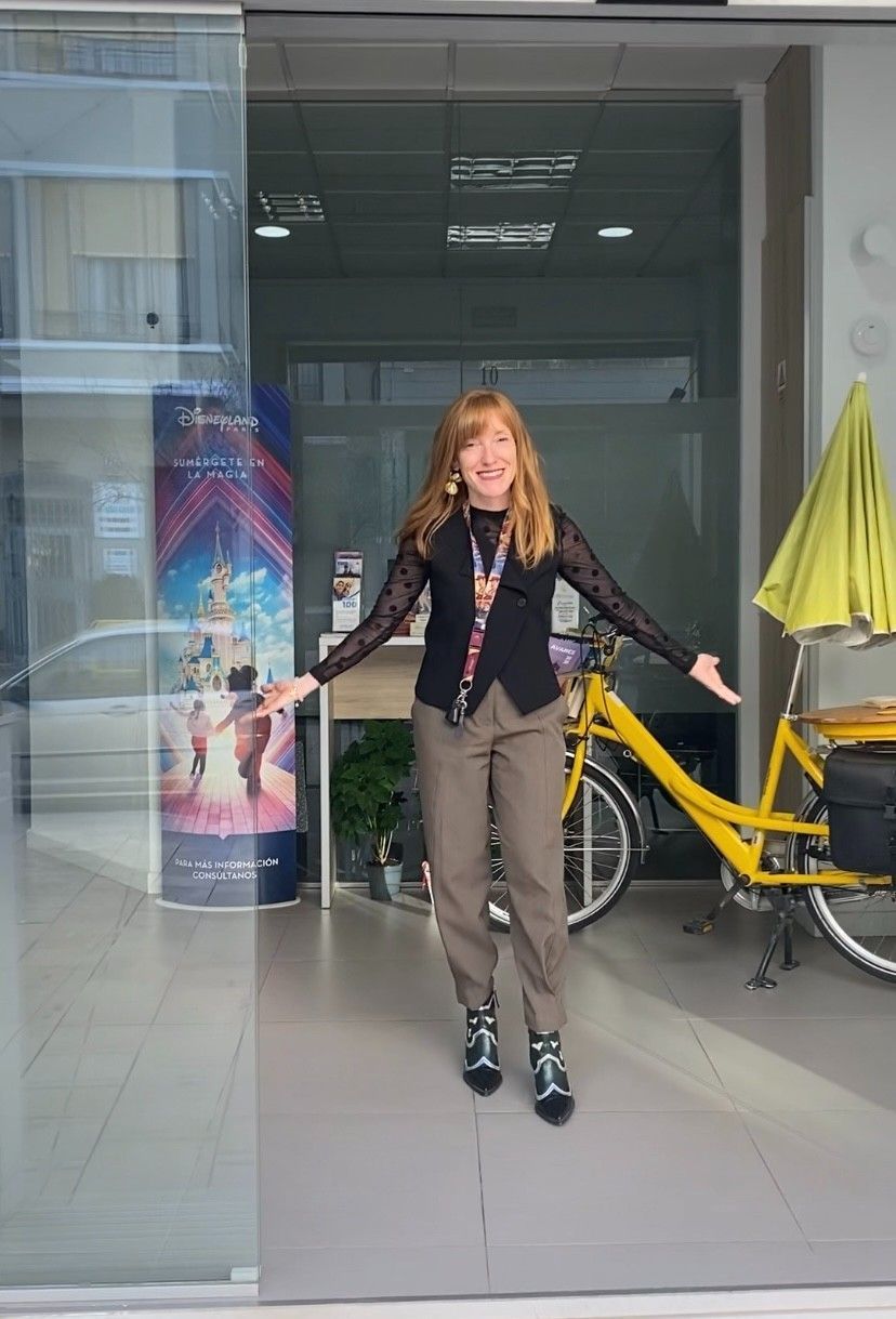 Una persona de pie en el umbral de una puerta de cristal, junto a una bicicleta amarilla con un paraguas amarillo.