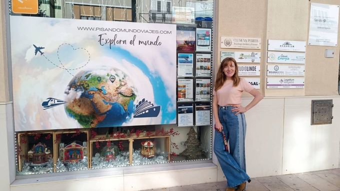 Mujer posando junto a un póster con temática terrestre y una vitrina con globos terráqueos en un aula.