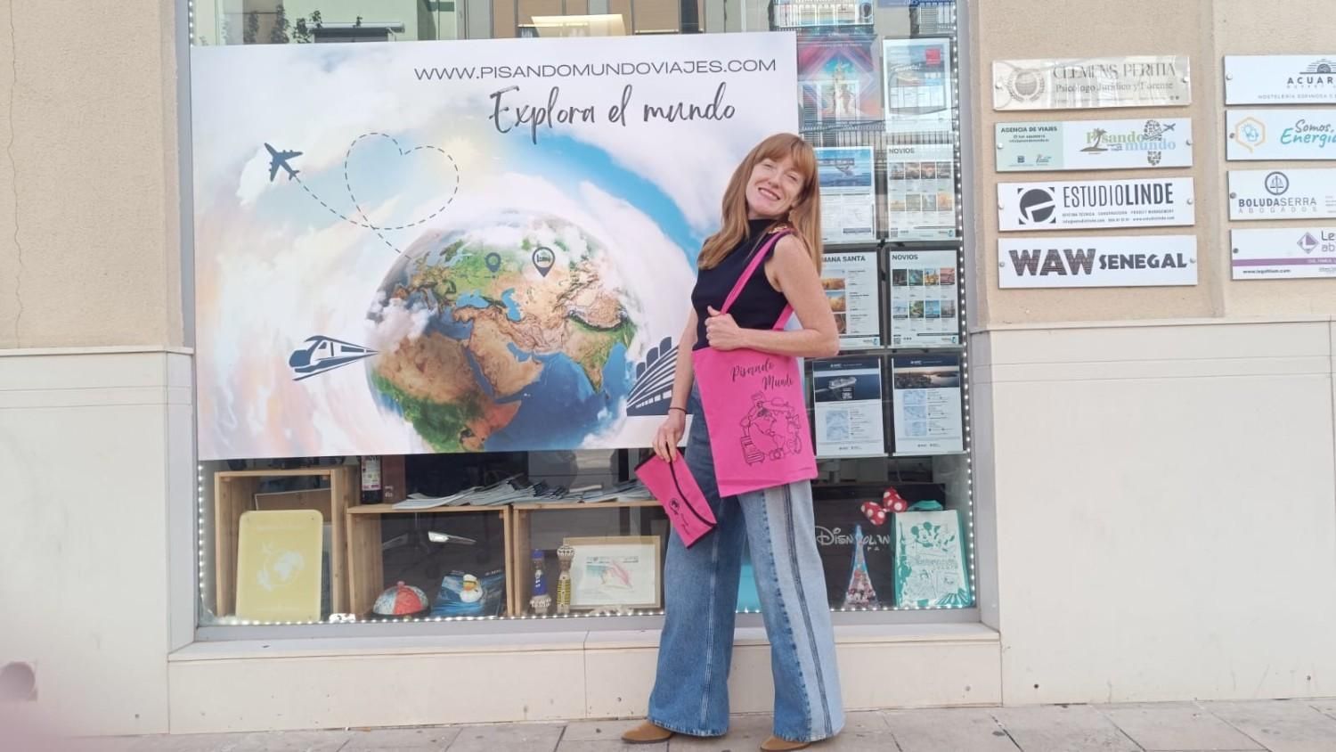 Mujer vestida de rosa posando junto a un mural de la Tierra y pájaros en el escaparate de una acera.