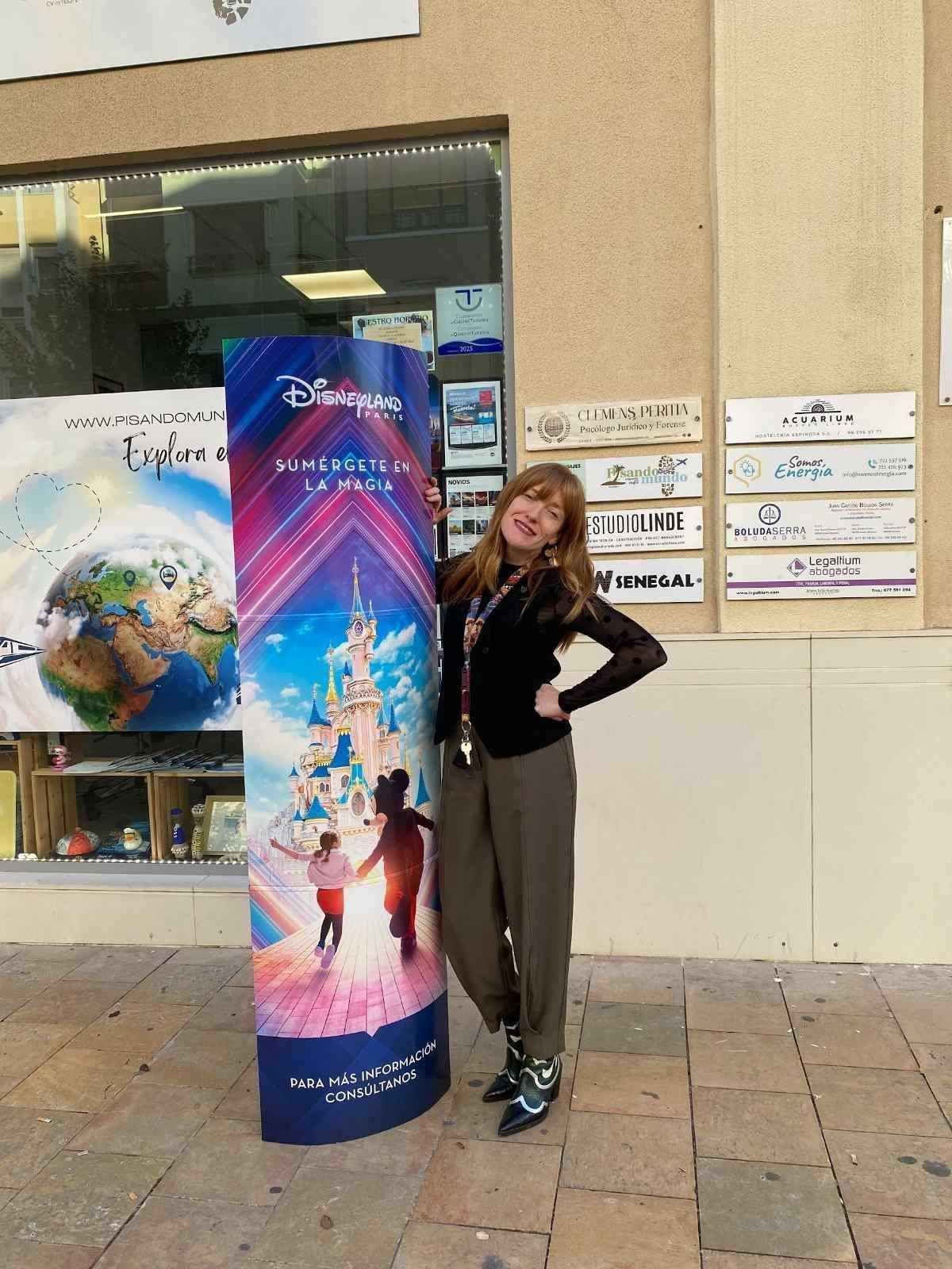 Mujer de pie junto a un colorido cartel publicitario en el exterior de un edificio.