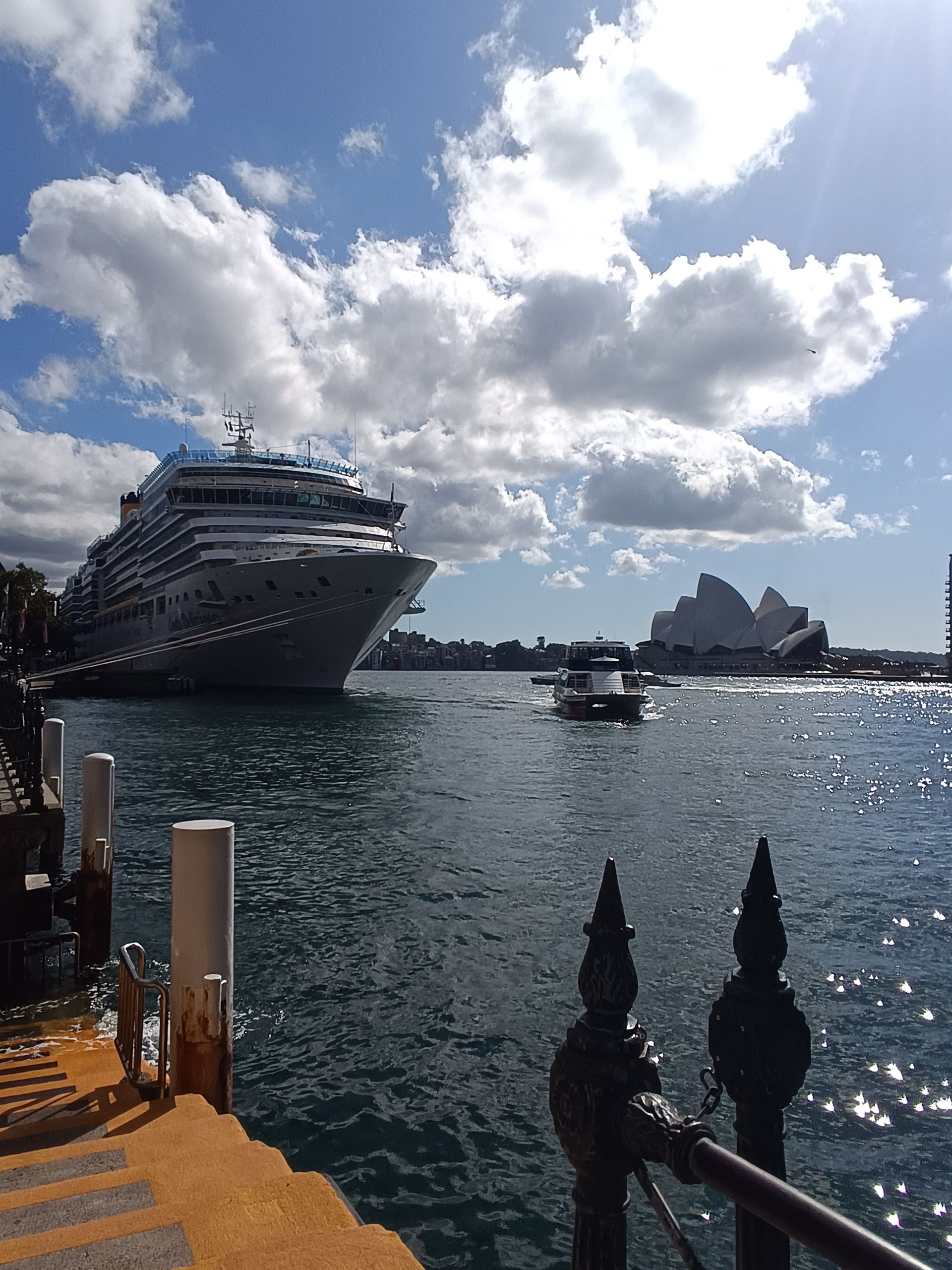 Un gran crucero blanco atracó en un puerto, con gente caminando por el muelle bajo un cielo nublado.