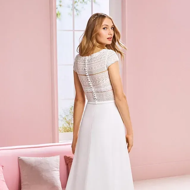 Una mujer con un vestido blanco está parada frente a un sofá rosa.