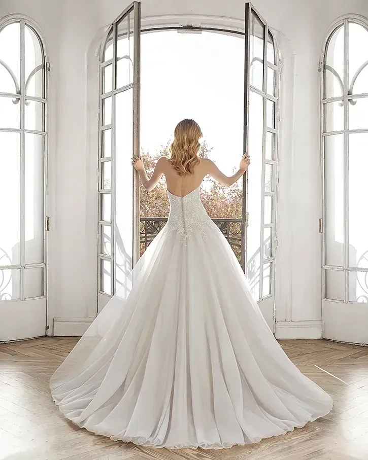 Una mujer con un vestido de novia está parada frente a una ventana.