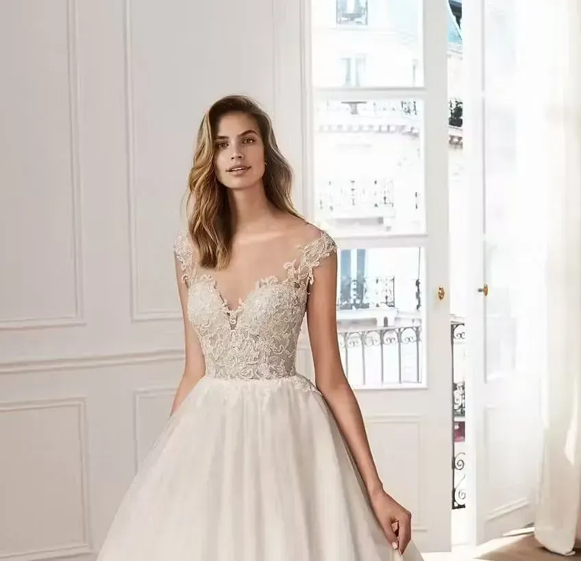 Una mujer con un vestido de novia blanco está parada frente a una ventana.
