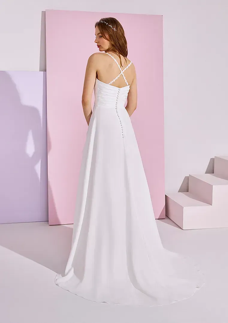 Una mujer con un vestido de novia blanco está parada frente a una pared rosa.