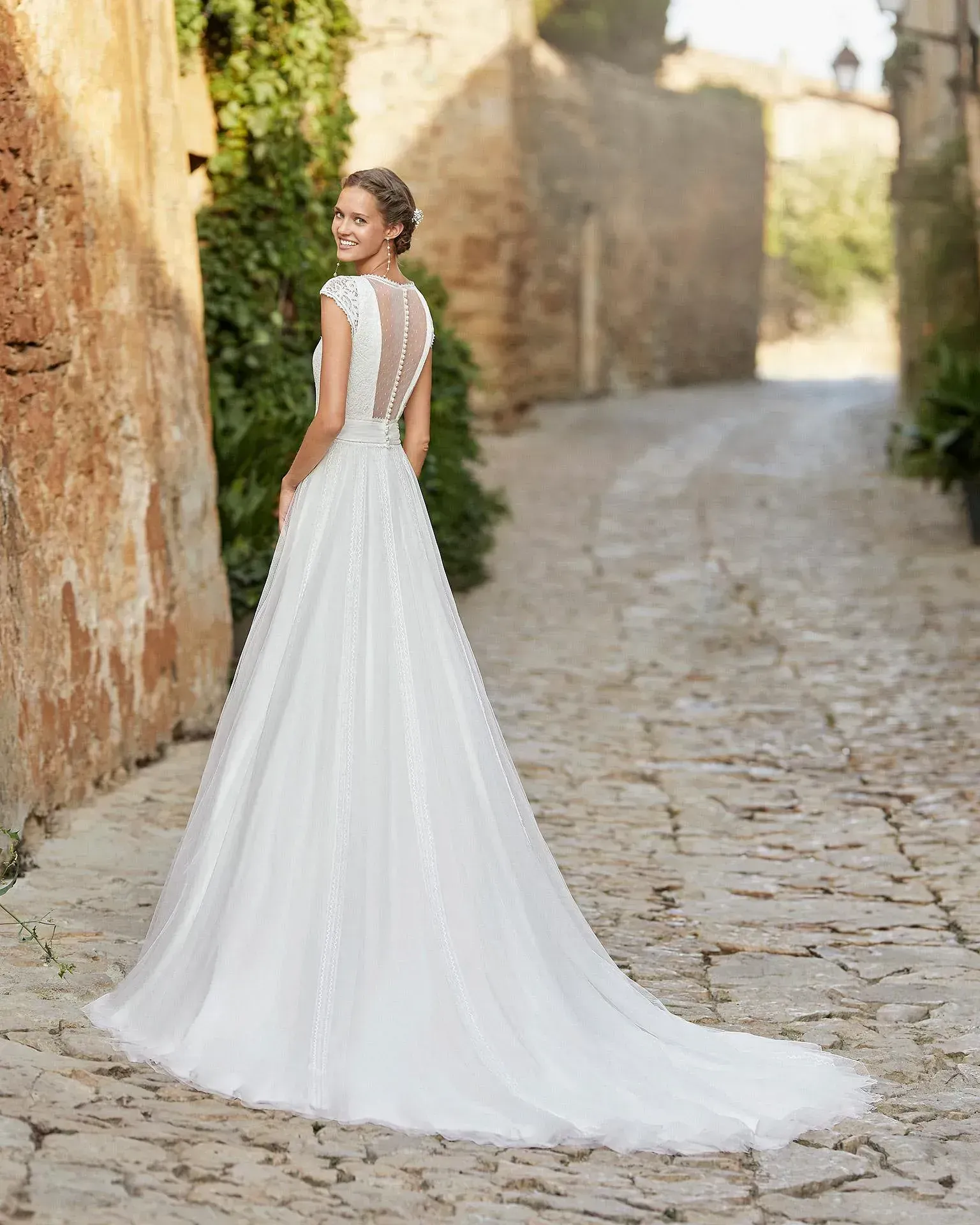 Una mujer con un vestido de novia blanco está parada en una calle adoquinada.