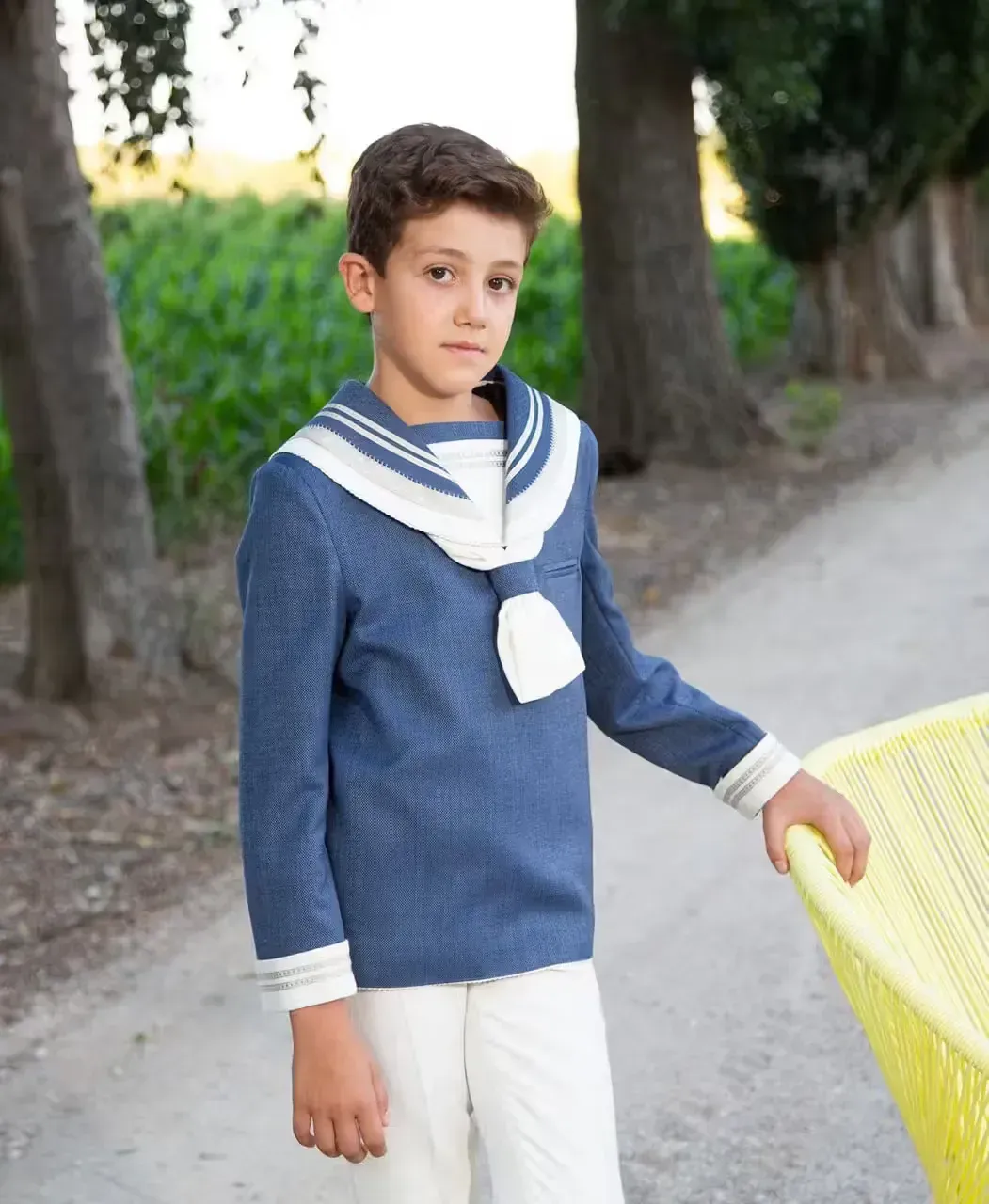 Un niño con traje de marinero se encuentra junto a una canasta amarilla.