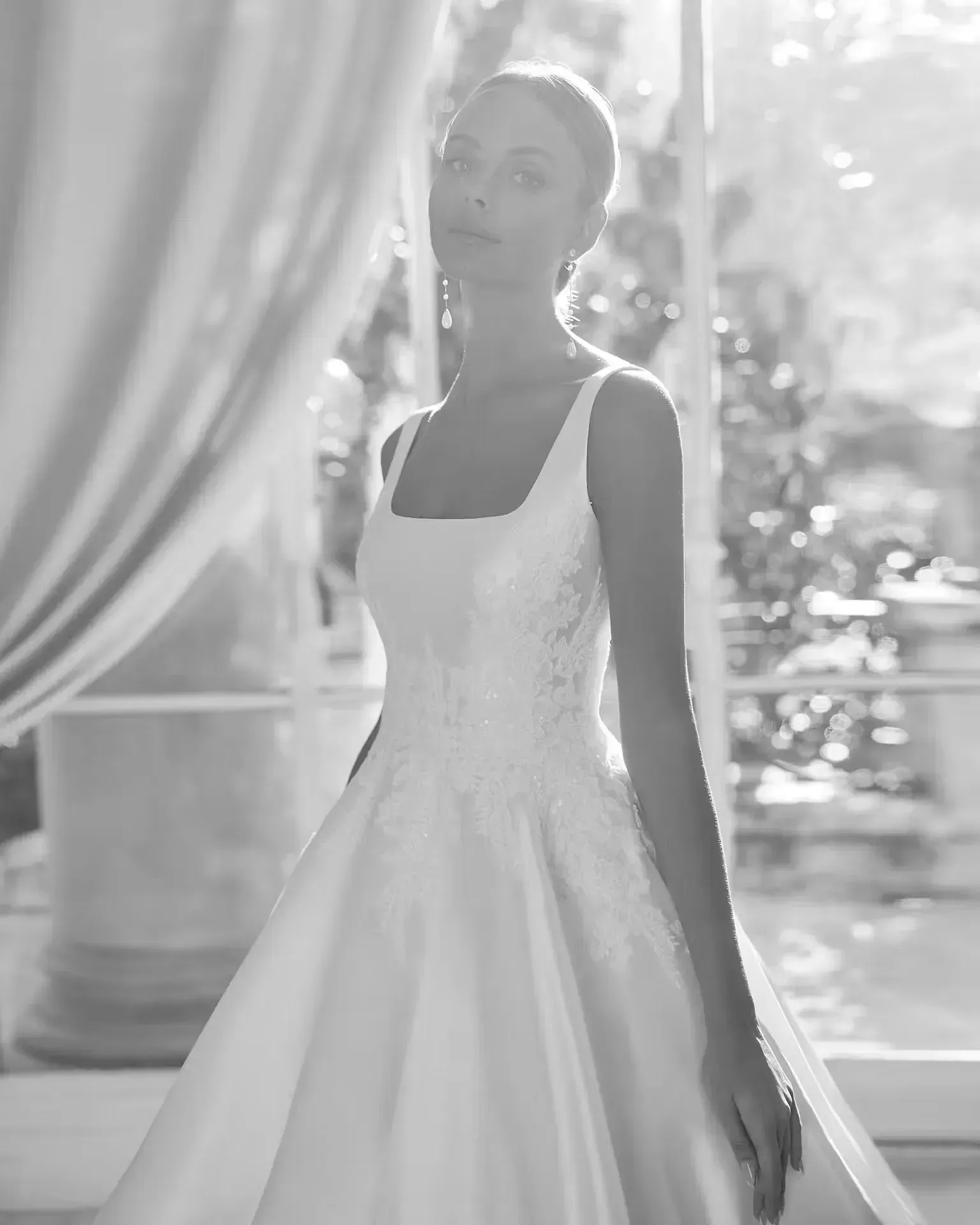 Una fotografía en blanco y negro de una mujer con un vestido de novia parada frente a una ventana.