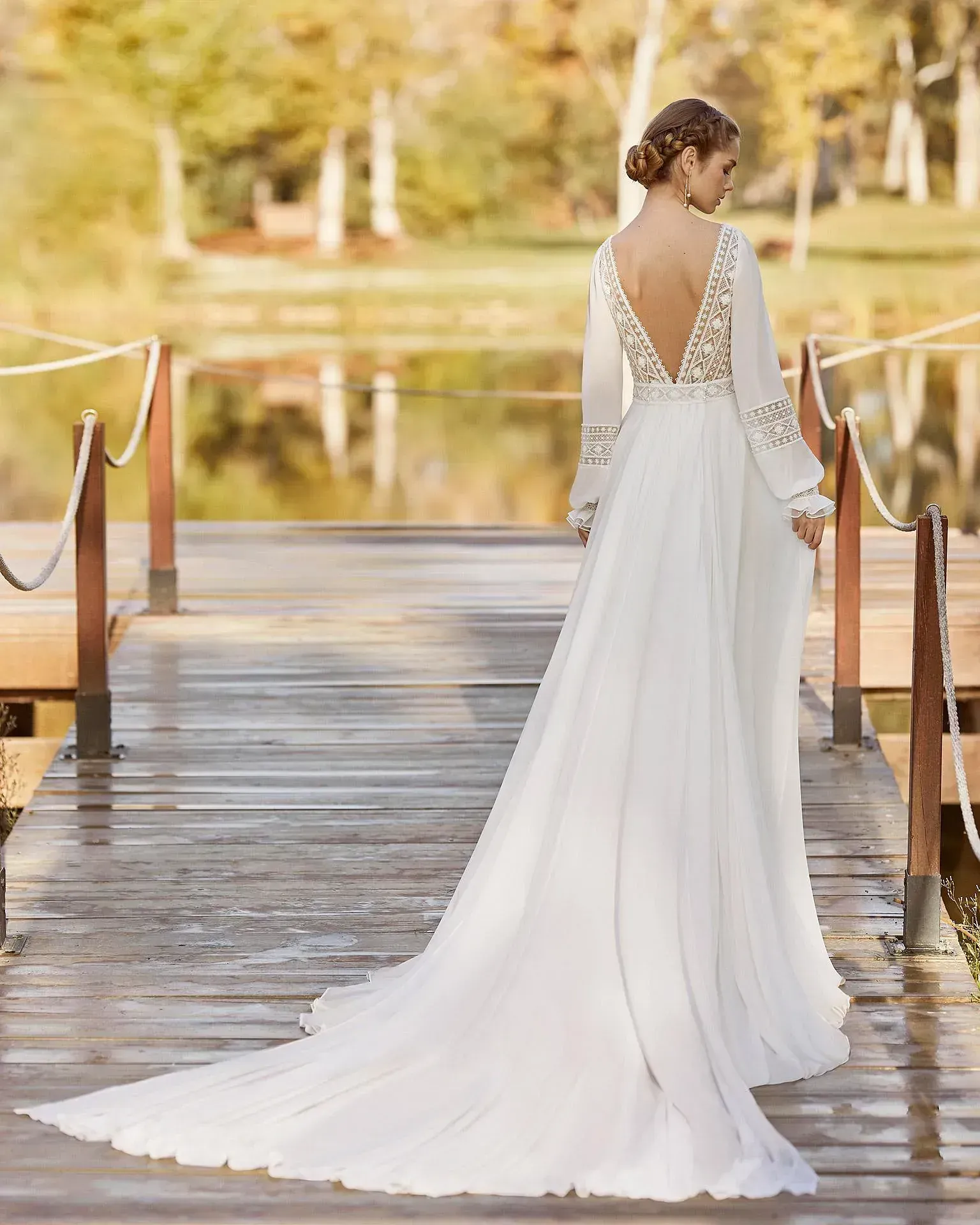 Una mujer con un vestido de novia blanco está parada en un muelle de madera.