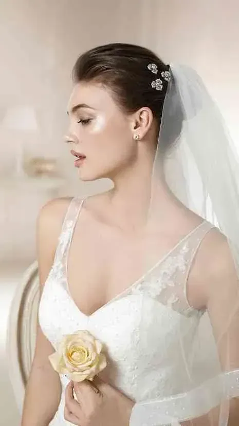 Una mujer con vestido de novia y velo sostiene una rosa.
