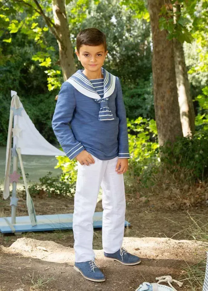 Un niño pequeño que viste una camisa azul y pantalones blancos está parado en el bosque.