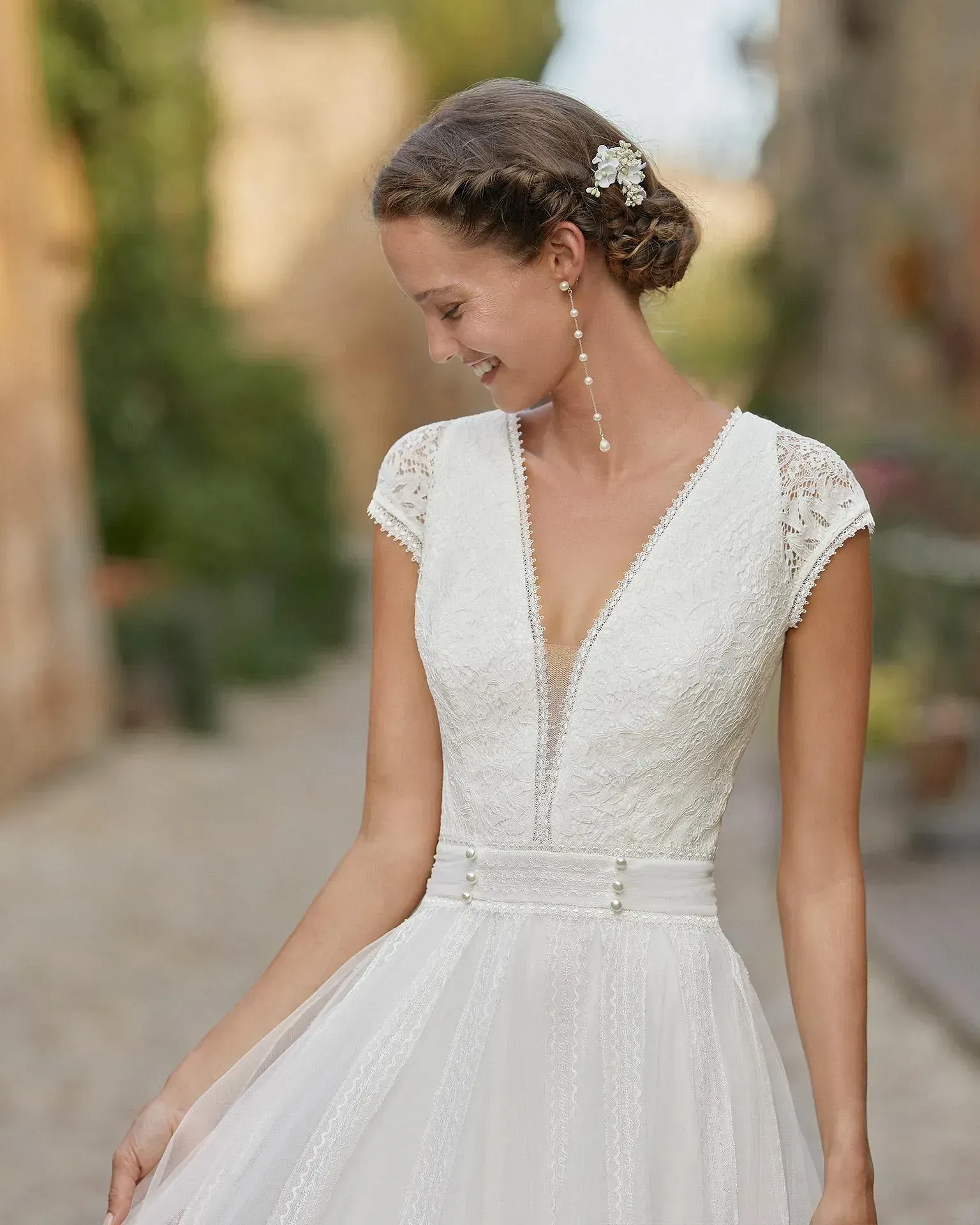 Una mujer lleva un vestido de novia de encaje blanco y pendientes.