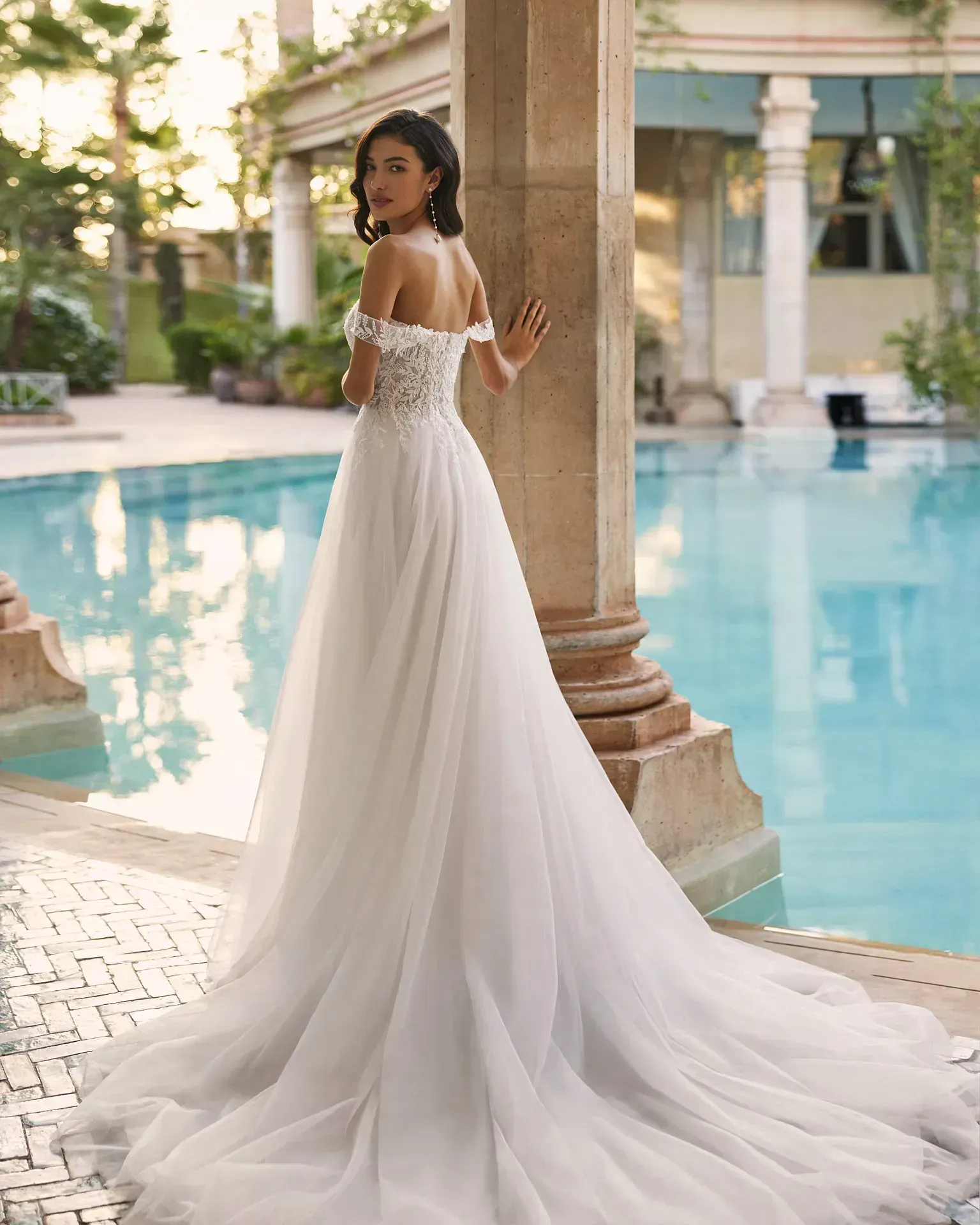 Una mujer con un vestido de novia blanco está de pie junto a una piscina.