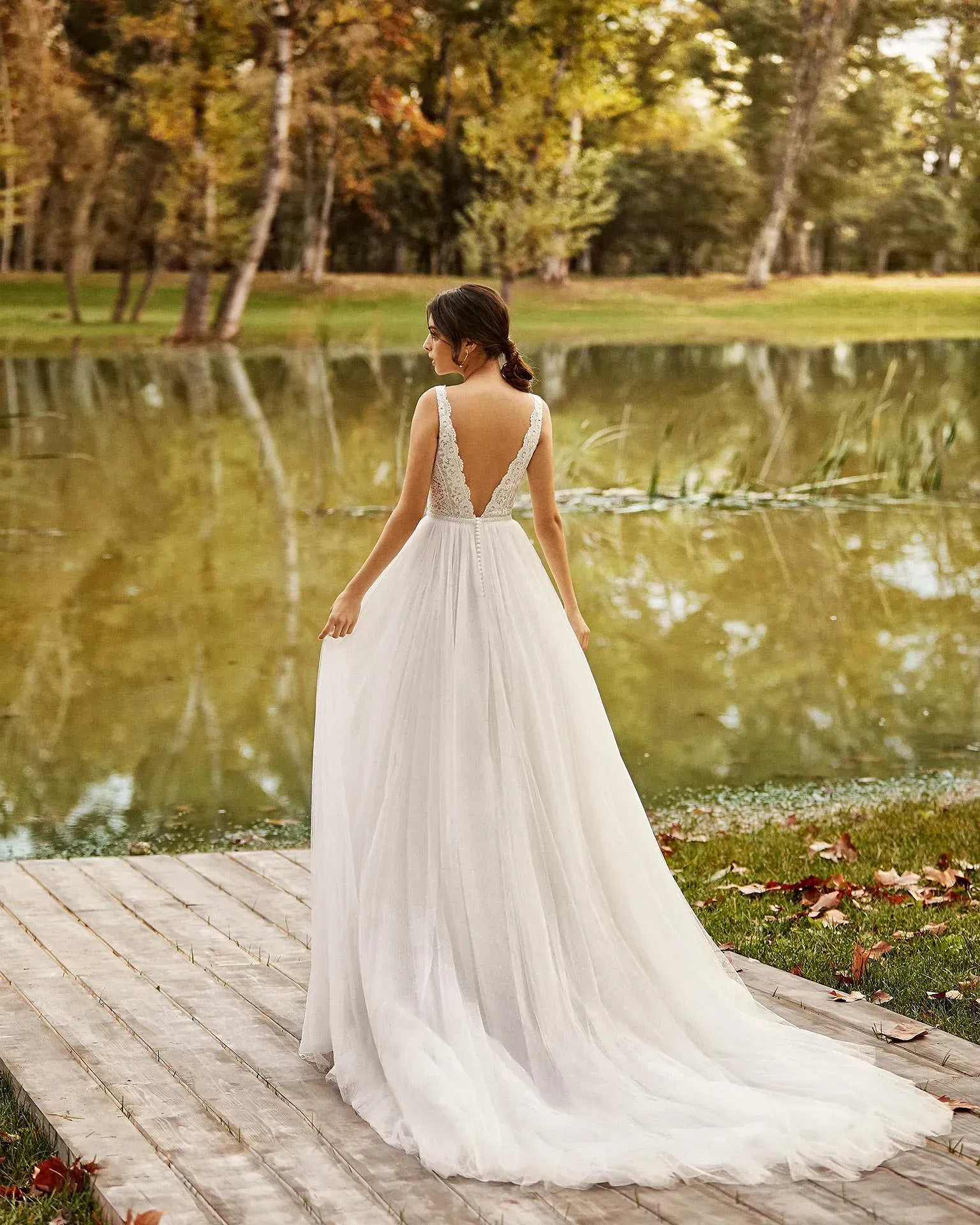 Una mujer con un vestido de novia está parada en una pasarela de madera junto a un lago.