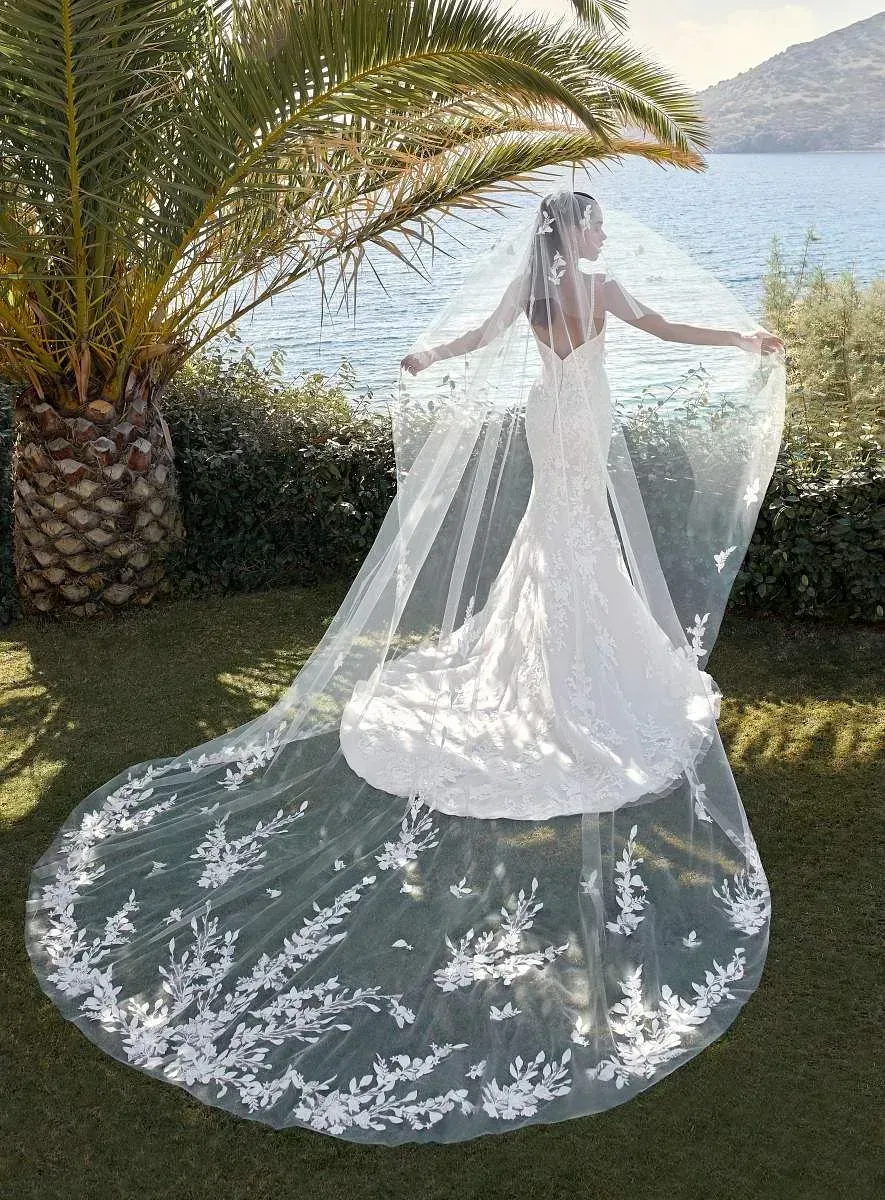 Una mujer con vestido de novia y velo está parada frente a una palmera.