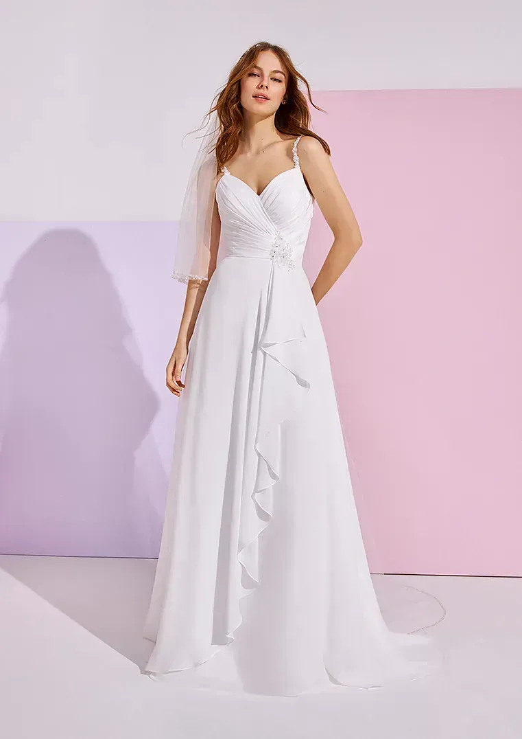 Una mujer con un vestido de novia blanco está parada frente a una pared rosa y violeta.