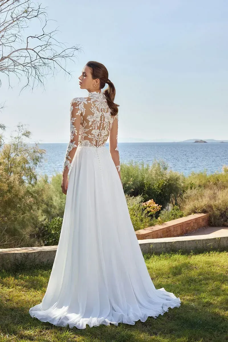 Una mujer con un vestido de novia blanco está parada en el césped cerca del océano.